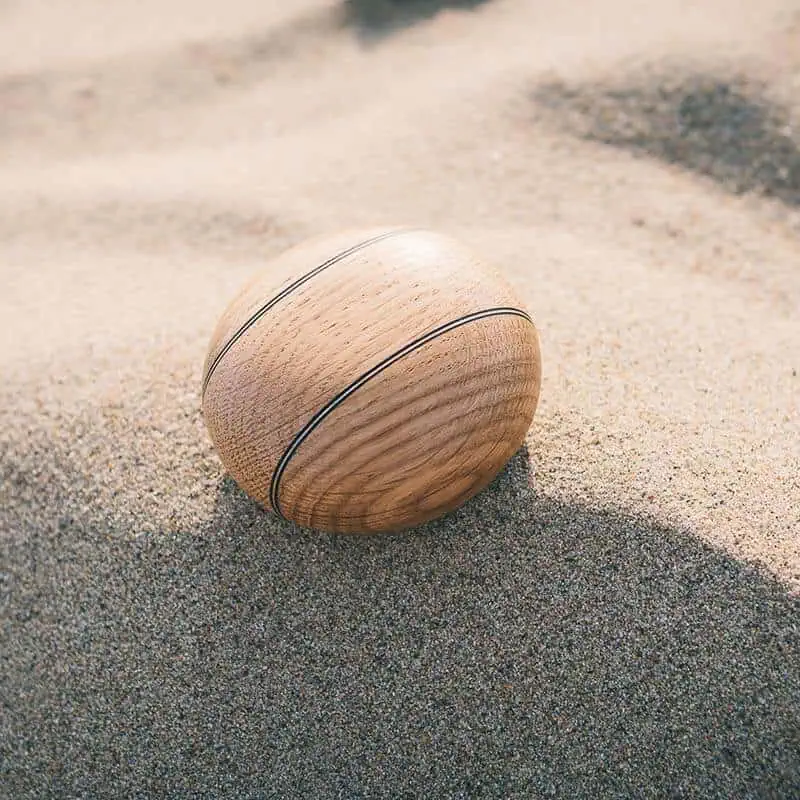 Houten urn met donkere dubbele lijnen, liggend op een zonnig zandstrand.