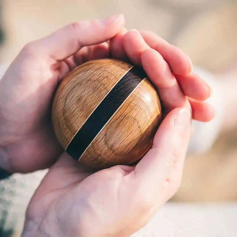 Houten urn met donkere brede streep, vastgehouden door twee handen.