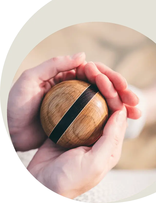 Sfeerafbeelding van kleine ronde houten urn met donkere brede streep, vastgehouden door twee handen.