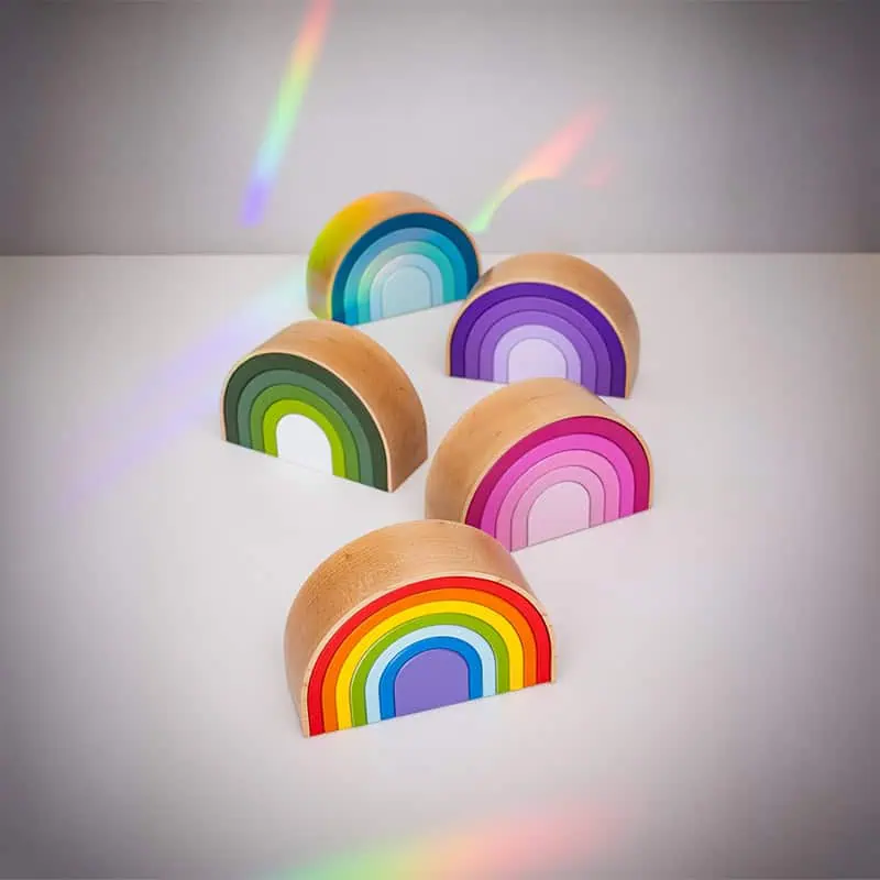Vijf houten halfcirkelvormige urnen Rainbow in alle kleuren gegroepeerd op een witte ondergrond, met kleurrijke regenboogkleurige lichtreflecties op de achtergrond