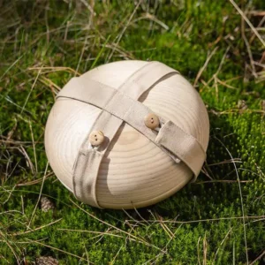 Ronde houten Still urn met beige stoffen riem en houten knopen, rustend op mos en droog gras