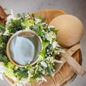 Geopende Still urn op een houten boomschijf met blauwe dekentje, naast de ronde houten deksel, omringd door een krans van witte en groene bloemen