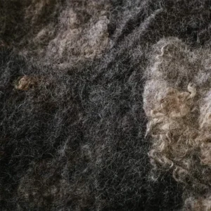 Close-up van de gevilte donkergrijze wol waarin zacht licht de structuur en lichte wolkrullen laat zien