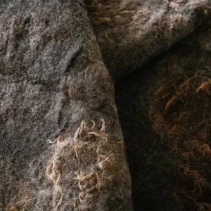Close-up van een vouw in de gevilte donkergrijze wol met lichte wolkrullen langs de rand