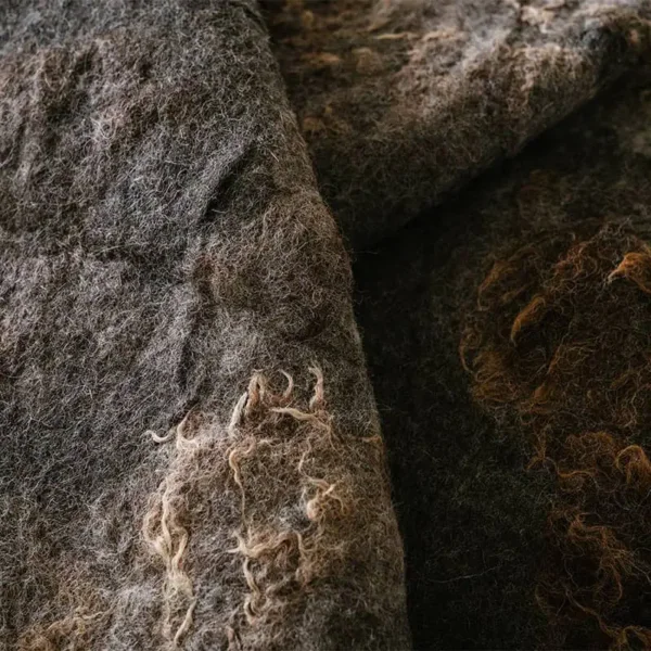 Close-up van een vouw in de gevilte donkergrijze wol met lichte wolkrullen langs de rand