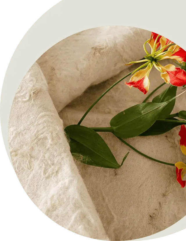 Detail van een handgemaakte wollen wade van 100% biodynamische wol, met een rood-gele gloriosa erop; de zachte, natuurlijke structuur van de vilten wol is duidelijk zichtbaar.