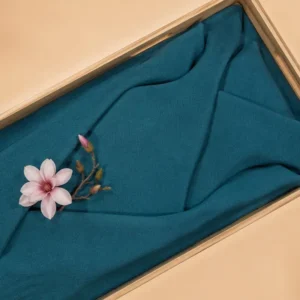 Petrol lijkwade van fijn geplooid Egyptisch katoen, gedrapeerd in een lichte houten kist, met een roze magnoliabloem op een takje erop.