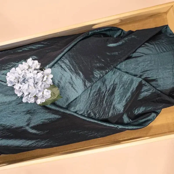 Aqua Blauw lijkwade van glanzende taft, gedrapeerd in een lichte houten kist, met een blauwpaarse hortensia erop.