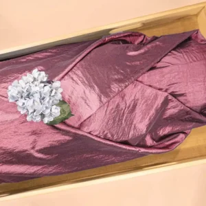 Roze lijkwade van glanzende taft, gedrapeerd in een lichte houten kist, met een blauwpaarse hortensia erop.