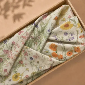 Dubbele wade met een aquarelprint van veldbloemen in roze, geel, oranje en paars op een cremekleurige ondergrond, gevouwen in een lichte houten bak.