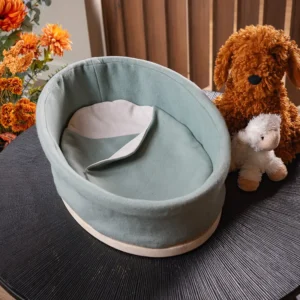 Heaven uitvaartmandje in zachtgroen op een donkere tafel, met oranje bloemen links en een knuffelhond en knuffellam rechts