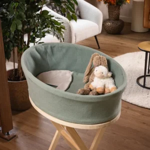 Heaven uitvaartmandje in zachtgroen op een houten standaard in een woonkamer, met een knuffelkonijn en knuffelschaap in de bak
