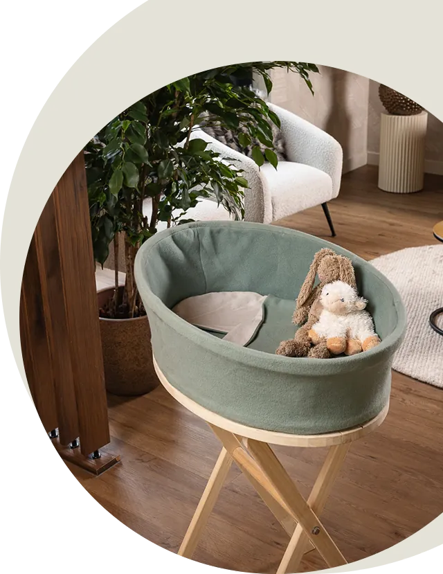Heaven uitvaartmandje in zachtgroen op een houten standaard in een woonkamer, met een knuffelkonijn en knuffelschaap in de bak, in een ronde uitsnede