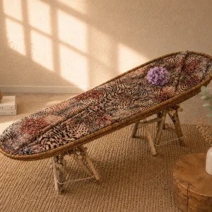 Sfeerfoto van de jacquard lijkwade met safariprint in een rieten baar op houten schragen, in een zonverlichte kamer met droogbloemen, boeken en een vaas met eucalyptus.