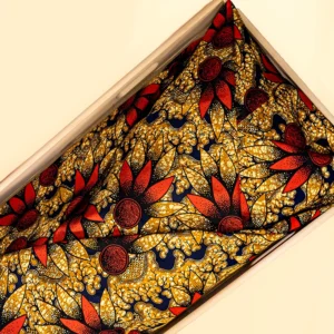 Lijkwade met batikprint van rode bloemen op een ondergrond van okergeel en donkerblauw, gevouwen in een lichte houten bak.